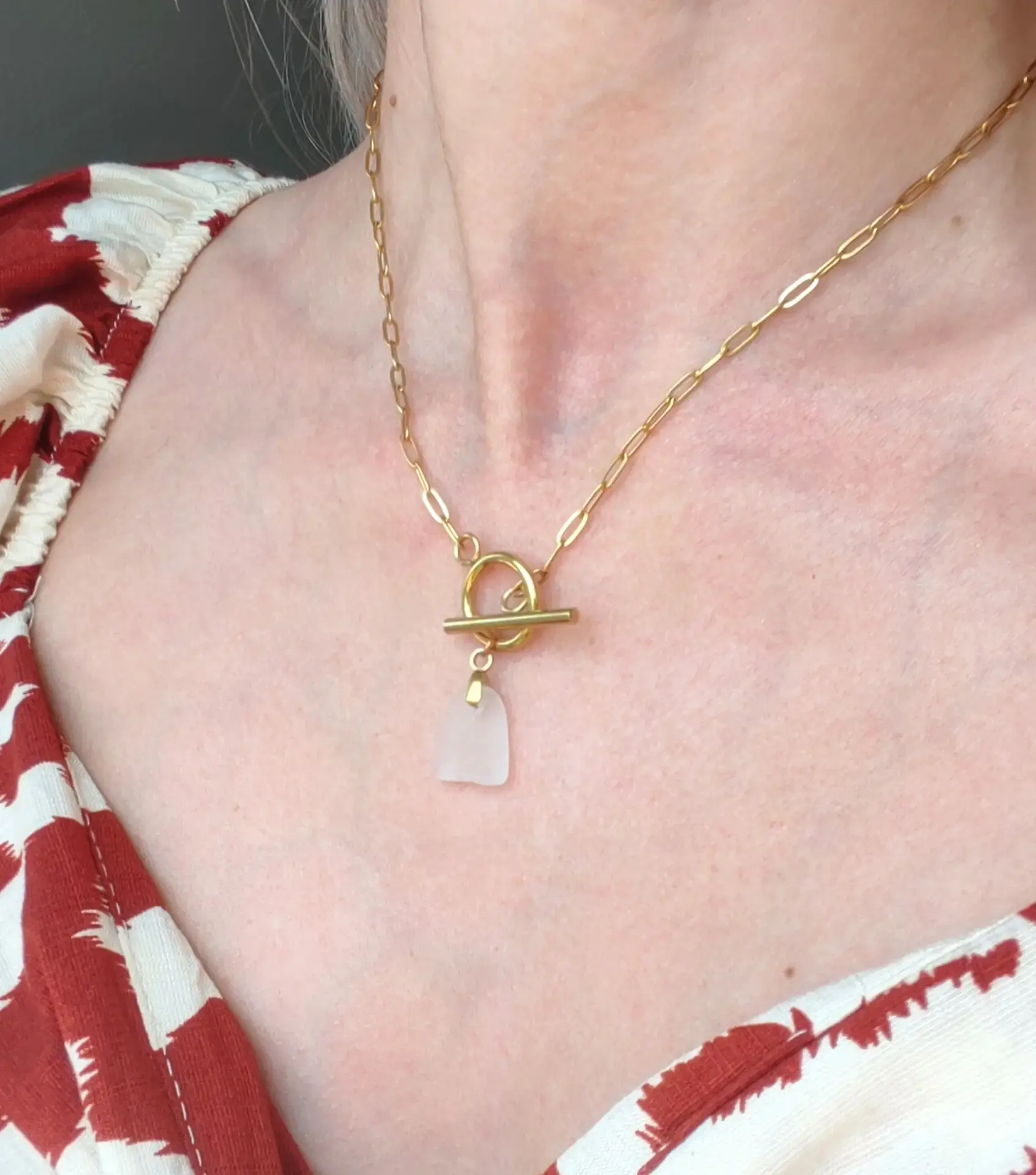 Le collier Celestun doré porté sur un haut rouge et blanc, son éclat de verre de mer givré posé sous le fermoir